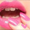 Close-up of a mouth with pink lips and teeth, fingers with pink nails holding the lower lip, and a small pink heart tattoo on a finger.