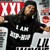 A pixelated static image shows a person in a black hoodie with white text, holding a red and white sign with 'XOXO' visible, against a blurred background with partial text elements.
