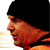 Pixelated profile view of a person wearing a black beanie, with orange and brown tones on the face and neck, against a white and yellow striped background.