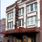 Pixelated image of a multi-story building with large windows and a brown facade, viewed from a low angle against a light sky.