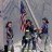 Pixelated static image showing three figures in a group, one holding a tall object, against a muted background.