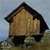Pixelated static image of a brown house with a dark roof, black base, and light-colored walls, set against a blue sky background.