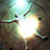 Pixelated image with bright central light, green and brown tones, and scattered dark spots on a muted background.