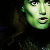 Pixelated green-toned face with wide eyes and open mouth against dark background, partially cropped on left side.