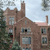 Pixelated image of a brown brick building with multiple windows, chimneys, and a light blue sky background.
