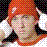 Pixelated close-up of a person with red hair and light skin, wearing dark clothing against a checkered background.