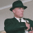 Static 48x48 pixel icon of a man in dark green attire with a matching hat, white shirt collar visible, and light skin tone against a gray background.