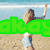 A pixelated beach scene with a person in light blue shorts and dark top raising one arm, overlaid by bright green text.
