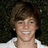Pixelated portrait of a smiling person with brown hair wearing a white shirt against dark foliage background.
