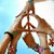 A person in a brown outfit forms a peace sign with hands, wearing pink wristbands and green sleeves against a light blue background.