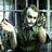 A character with green hair and white face paint stands behind metal bars, holding a small object in one hand while the other hand is raised near their head.