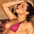 Pixelated static image of a woman in a pink bikini top with dark hair, lying down on a brown background.