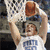 A basketball player in a white jersey with blue text dunks a ball through a hoop, surrounded by light blue containing text and symbols