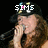 A person with long brown hair wearing a black cap with colorful dots sings into a microphone, with text overlays changing across frames.