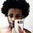Pixelated image of a person with dark curly hair holding a white smartphone against a light background.