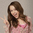 A pixelated image of a person with long brown hair making a peace sign, set against a pink background with text overlays.