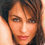 A pixelated close-up of a person's face with brown hair, light skin, and red lips, set against a light background.