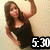 A pixelated image of a woman with long brown hair wearing a black dress, holding her right arm raised in a pose against a light beige background.