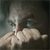 A pixelated image shows a person with light skin holding a syringe near their face against a dark background.