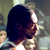 Pixelated image of a person with dark hair viewed from the side, wearing a light-colored shirt against a blurred background.