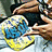 A pixelated image shows two hands holding a circular object with blue and yellow sections against a dark background.