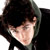 Pixelated static image of a person with dark hair and light skin, cropped to show upper face and shoulders against a white background.