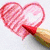 A heart-shaped icon with pink and white stripes, a wooden pencil tip at the bottom left, and a metallic silver background.