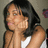 Pixelated image of a person with dark hair wearing a white top, hand near face, against a muted background with a small purple shape.