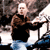 Pixelated static image of a person in dark clothing with light hair against a blurred background, likely from an old web archive or digital photo source.