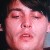 Pixelated close-up of a person's face with closed eyes, pinkish skin tone, and dark hair against a dark background.