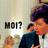 Pixelated image of a person with dark hair wearing a dark blue shirt, holding a white speech bubble containing the text 'MOI?' against a light background.