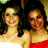 Two women in white and red strapless dresses smile together against a blurred green background.