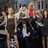 Group of people gathered around a table with one person holding a microphone, next to stylized text reading 'gossip girl' on black background.