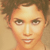 Pixelated close-up of a person's face with short curly hair, neutral expression, and light skin tone against a beige background.