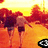 Two figures walk away from the viewer across an orange field under a yellow sky, with trees in the background.