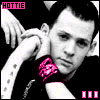 A black-and-white photo of a person with short dark hair resting their head on an arm, wearing a pink wristband and chain necklace, displayed in a