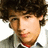 Pixelated close-up of a person with dark curly hair, light skin, and a red tie, wearing a dark jacket over a light shirt against a white background.