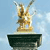 Pixelated golden statue of a figure holding a sword aloft on a dark pedestal against a light blue background.