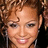 A pixelated close-up of a person with curly brown hair, light skin tone, and visible earlobe wearing small earrings.