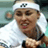 Static 48x48 pixel icon of a tennis player wearing a white headband with dark logo, white shirt, and black wristband, smiling with mouth open showing teeth, visible tattoos on neck and arm, against blurred background.