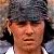 A pixelated close-up of a person wearing a dark gray fur hat with ear flaps, light brown skin, and a white shirt collar visible at the bottom edge.