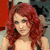 A woman with long red hair and blue eyes appears in a static image, wearing a black top.