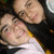 Two people in close physical proximity, one wearing a white top with yellow trim and the other in dark clothing, against a blurred background.