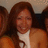A pixelated image shows a person with long brown hair wearing an orange top and white inner layer, seated among others in a group setting.