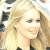 Static pixelated image of a person with long blonde hair and light skin, cropped to show upper body against a blurred background.