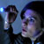 Pixelated image of two figures in dark clothing against a blue background, one figure holding a microphone near the other's face.