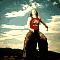 A woman in a red sleeveless top and brown pants performs a sequence of dynamic poses on a large dark rock against a cloudy sky background.