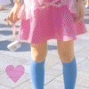 A person in a pink skirt and blue knee-high socks stands on a paved surface with a heart symbol below them.