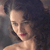 Pixelated close-up of a person with dark hair and red lips, wearing a dark strap over one shoulder against a dark background.