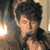 Pixelated static image of a person with dark tousled hair, light skin, and a dark jacket, set against a blurred background with warm and cool tones.